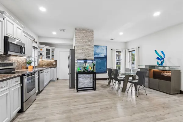 a kitchen with stainless steel appliances granite countertop a stove top oven a sink dishwasher a dining table and chairs with wooden floor