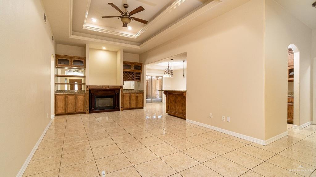 919 Hill Country Road Edinburg, TX 78539 - Photo 2 of 22 Spacious room featuring tile flooring, a tray ceiling with a ceiling fan, built-in cabinetry with mirrored backsplashes, a fireplace, and an archway leading to additional spaces