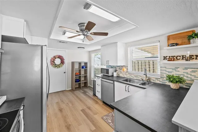 a kitchen with stainless steel appliances granite countertop a refrigerator a sink dishwasher a stove a dining table and chairs with wooden floor