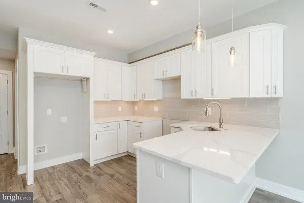 a kitchen with a sink dishwasher and white cabinets with wooden floor