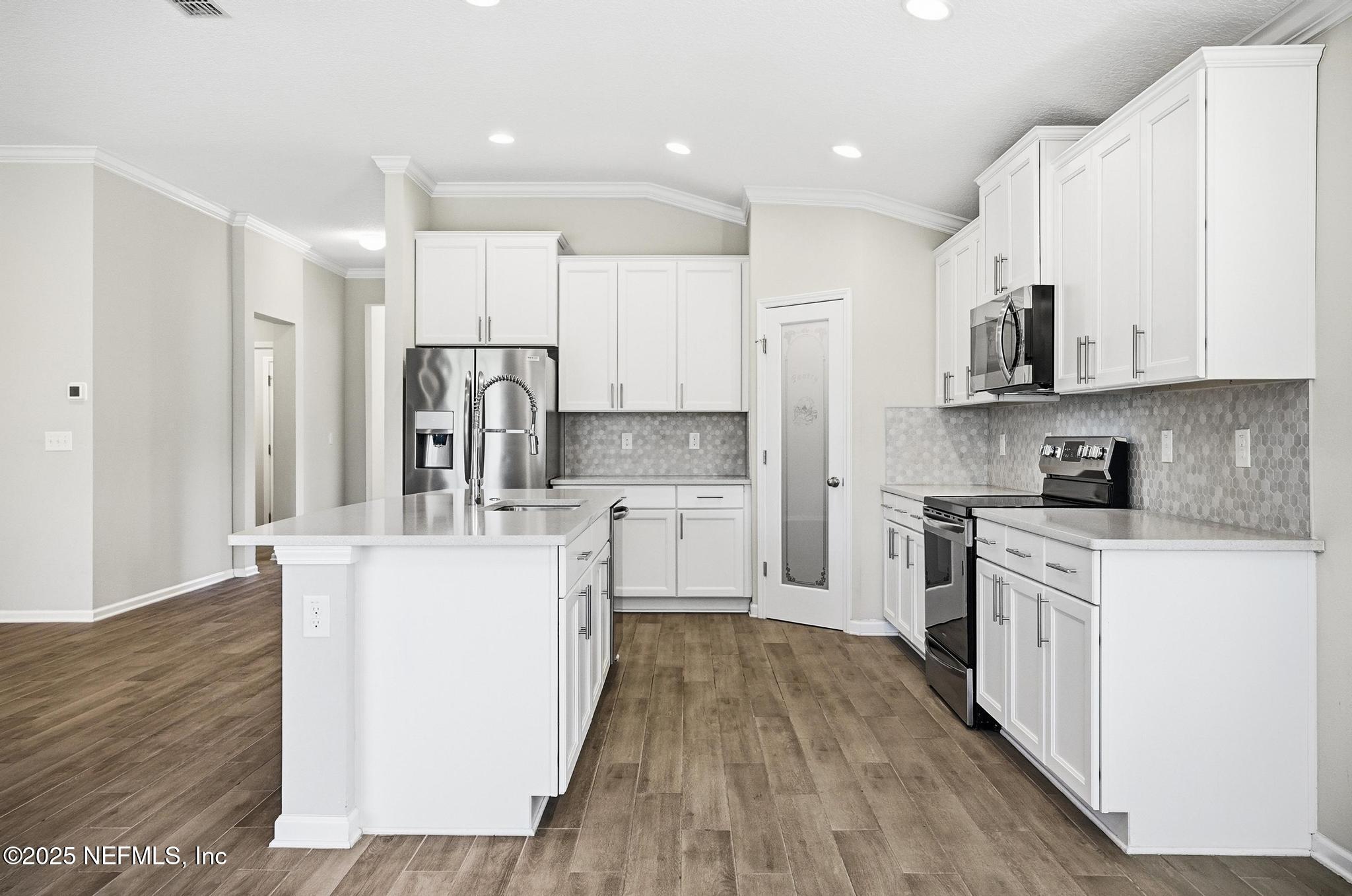 83 Hummingbird Court Palm Coast, FL 32164 - Photo 11 of 70 a kitchen with stainless steel appliances granite countertop a stove top oven a sink a refrigerator and white cabinets with wooden floor