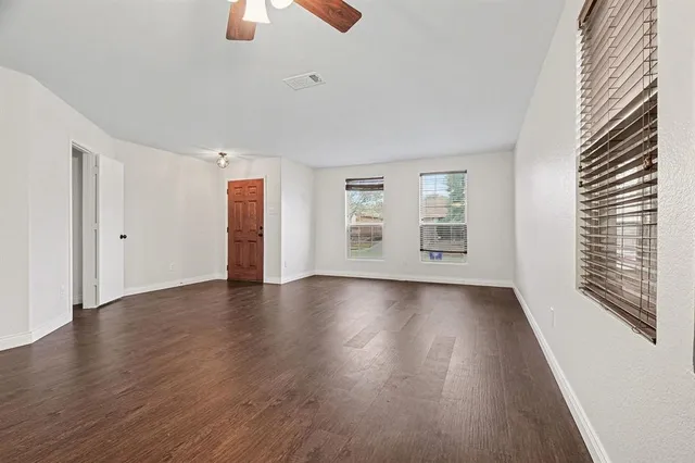 an empty room with wooden floor chandelier fan and windows