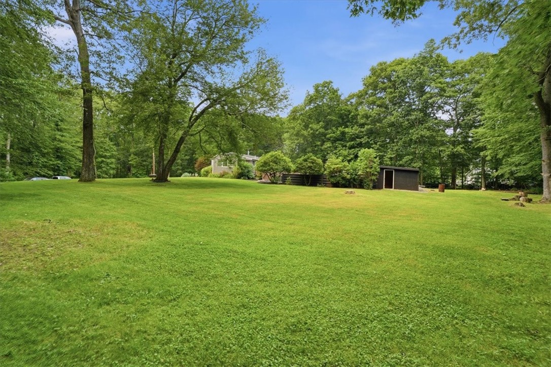214 Anan Wade Road Glocester, RI 02857 - Photo 47 of 50 Beyond the pool, decks, firepit, and outbuildings, the property continues with an expansive, beautifully open grassy side yard—a remarkable amount of usable outdoor space surrounded by mature trees and a peaceful wooded backdrop.