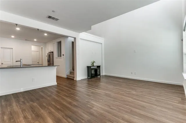 a view of an empty room and kitchen with wooden floor