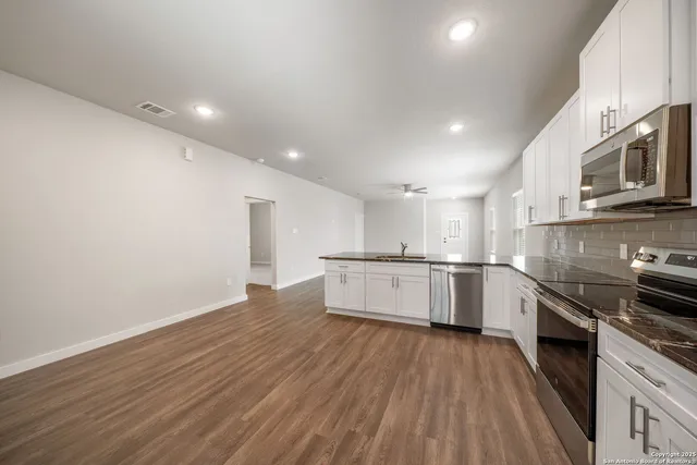 a large kitchen with granite countertop a stove top oven a sink dishwasher and white cabinets with wooden floor