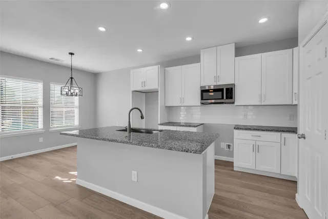 a kitchen with stainless steel appliances granite countertop a sink a stove and white cabinets with wooden floor