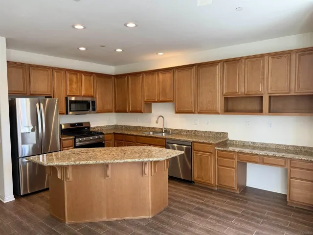 a kitchen with stainless steel appliances granite countertop a stove a sink dishwasher a refrigerator and a microwave oven with wooden floor