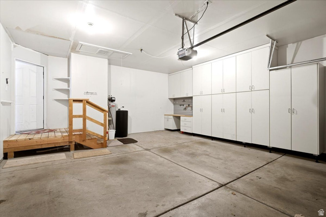 1089 West 2325th Street North Layton, UT 84041 - Photo 36 of 40 Integrated garage featuring extensive white cabinetry, a built-in workbench, an automatic garage door opener, a wooden entry platform with railing, and a side access door