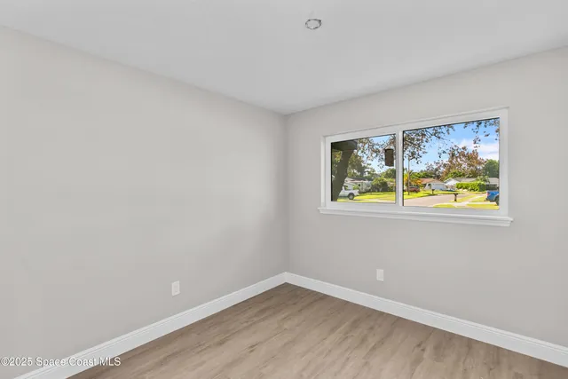 a view of an empty room with window and wooden floor