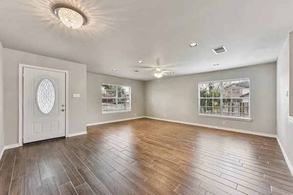 an empty room with wooden floor chandelier fan and windows
