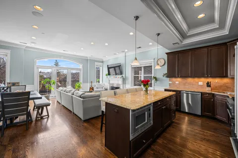 a kitchen with stainless steel appliances kitchen island granite countertop a refrigerator a stove a sink a dining table and chairs with wooden floor