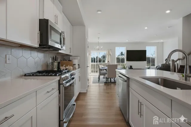 a kitchen with stainless steel appliances granite countertop a stove top oven a sink dishwasher and white cabinets with wooden floor