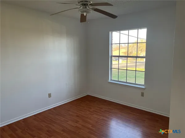 an empty room with wooden floor fan and windows