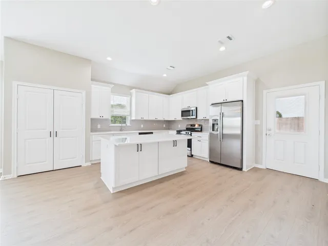 a kitchen with white cabinets appliances a sink and a window