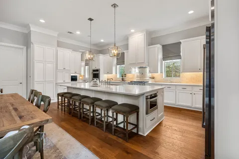 a kitchen with stainless steel appliances granite countertop a stove a sink a refrigerator and a dining table with wooden floor