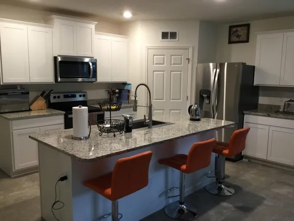 a kitchen with stainless steel appliances granite countertop a stove a sink a microwave a refrigerator and chairs