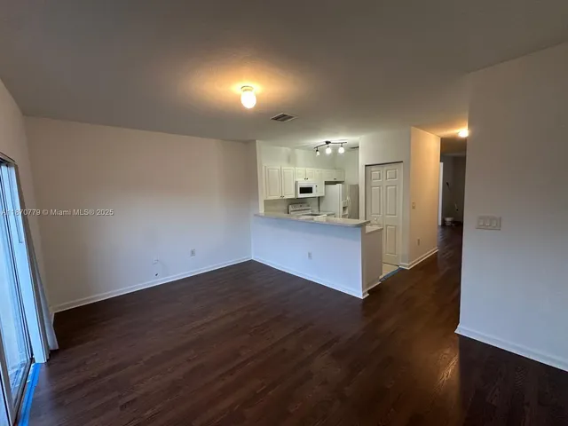 an empty room with wooden floor and a kitchen