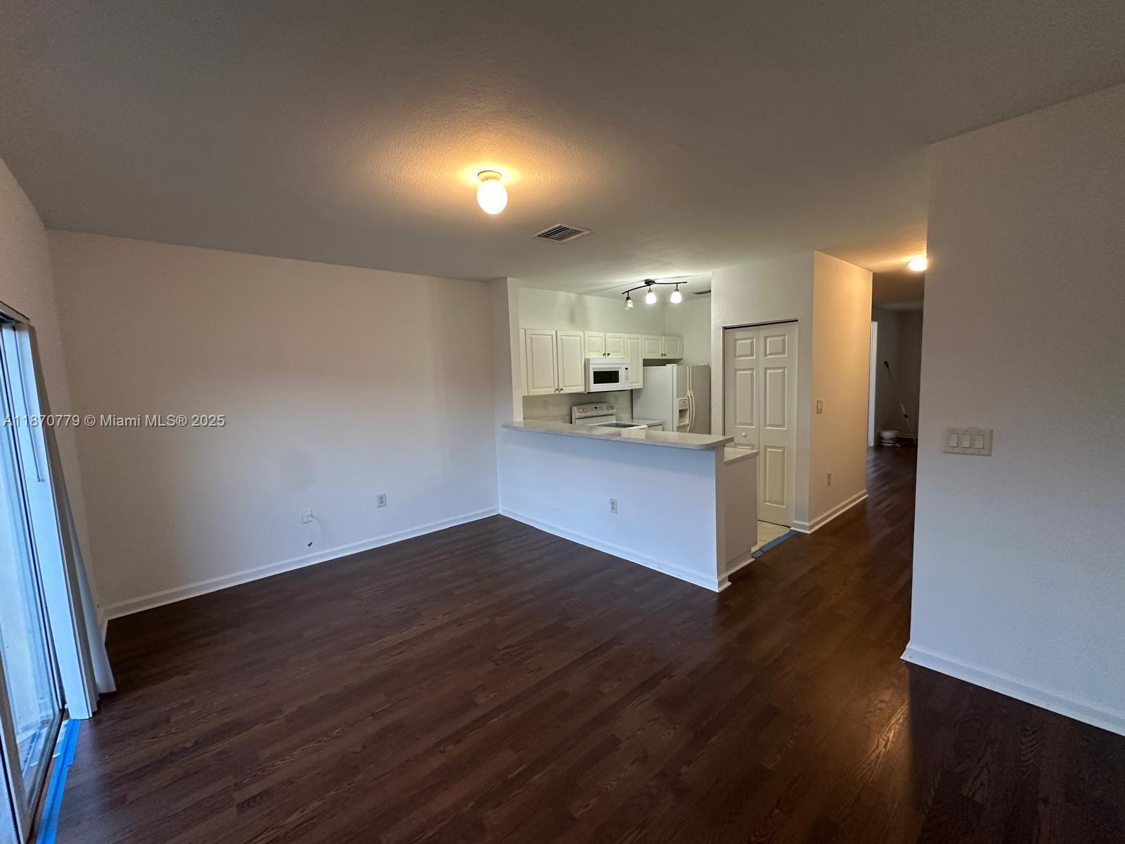 1555 Northeast 33rd Road, Unit 1042 Homestead, FL 33033 - Photo 18 of 19 an empty room with wooden floor and a kitchen
