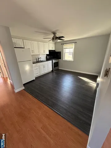 a view of empty room with wooden floor and kitchen view
