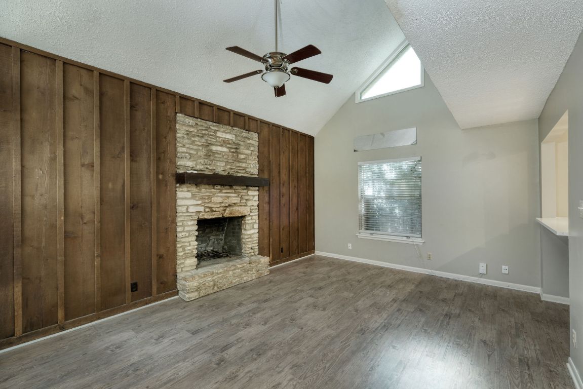 2711 St Edwards Circle, Unit 2 Austin, TX 78704 - Photo 4 of 17 Unfurnished living room with a textured ceiling, a ceiling fan, wood walls, wood finished floors, and high vaulted ceiling