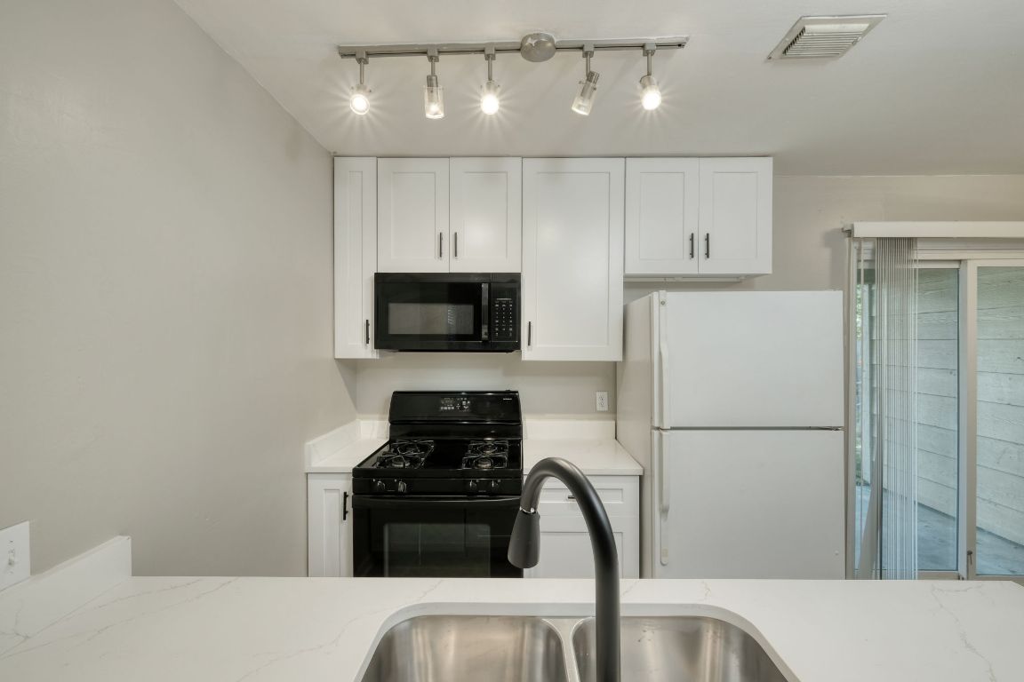 2711 St Edwards Circle, Unit 2 Austin, TX 78704 - Photo 8 of 17 Kitchen with black appliances, white cabinetry, rail lighting, and light stone countertops