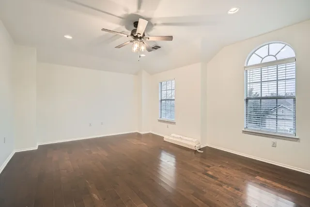 an empty room with wooden floor fan and windows