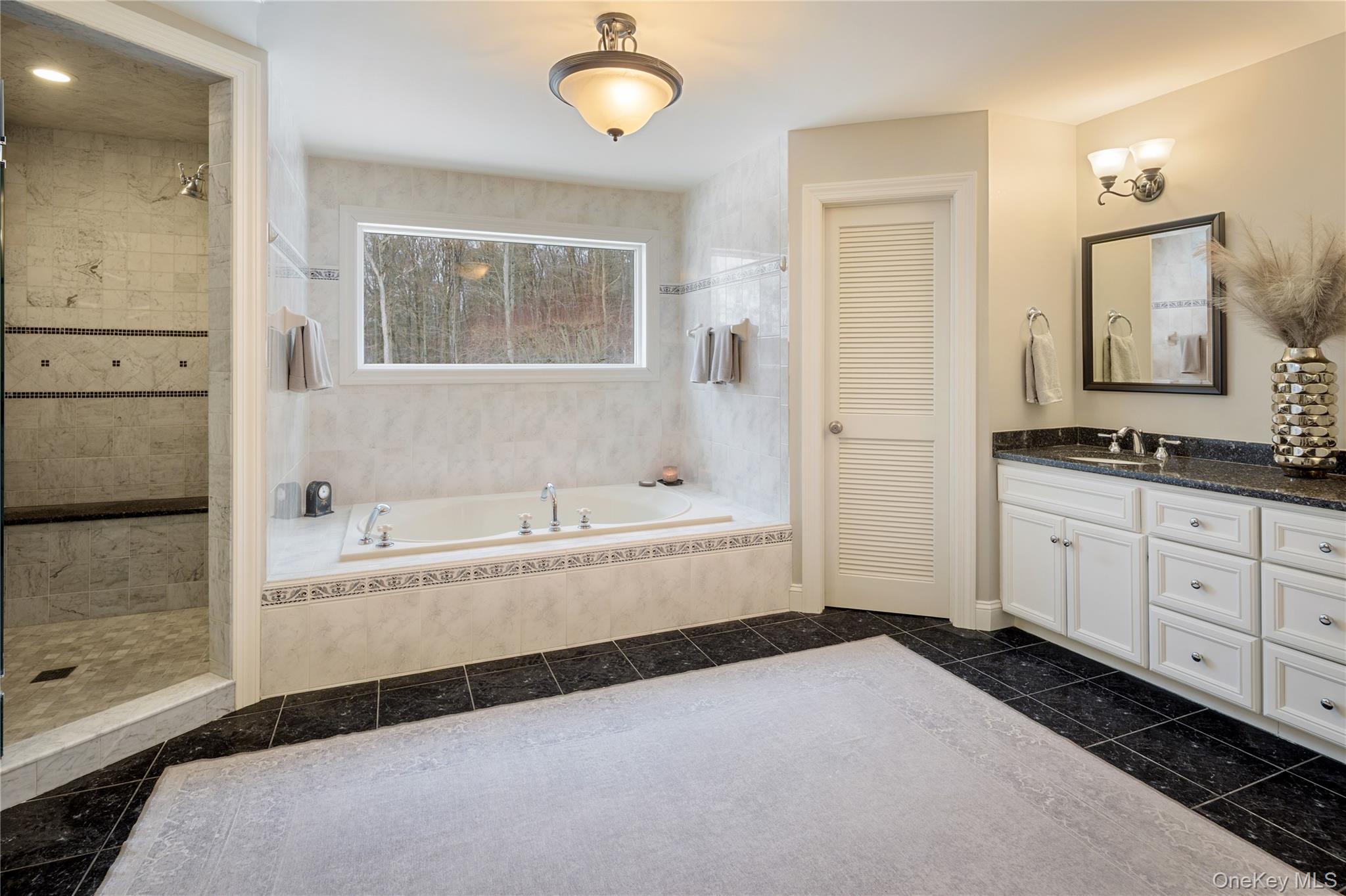 14 Adams Farm Road Katonah, NY 10536 - Photo 31 of 47 En-suite spa style primary bath features separate water closet, dressing vanity with pendant lighting, storage vanity with double sinks, jetted tub, separate oversized marble shower with stationary hand-held shower heads, built-in bench, glass door enclosure, product niche; wall sconces