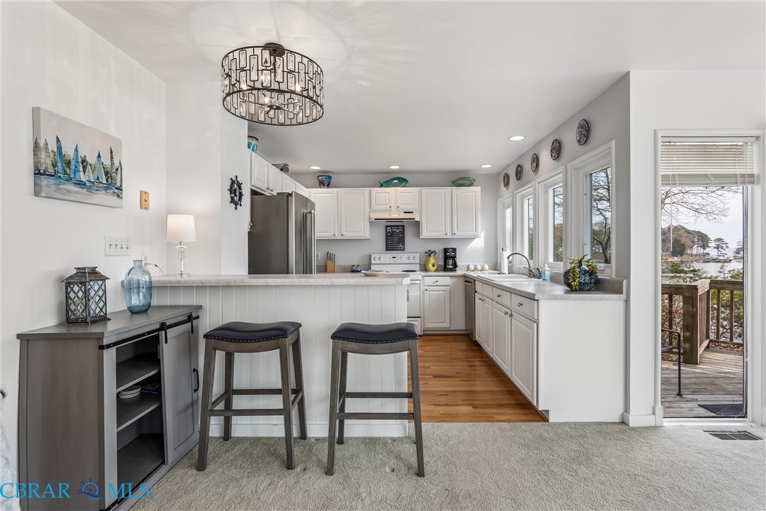 172 Sturgeon Creek Road Deltaville, VA 23043 - Photo 18 of 50 Kitchen featuring a kitchen bar, a peninsula, stainless steel appliances, white cabinets, and suspended lighting