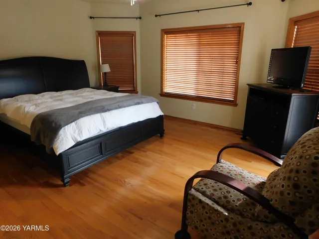 a bedroom with a bed and dresser with wooden floor