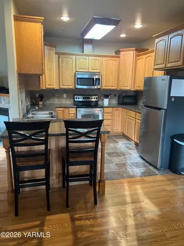 a kitchen with stainless steel appliances granite countertop a stove top oven a sink a dining table and chairs with wooden floor