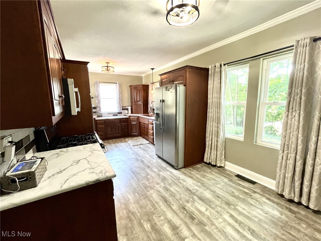 4440 Dryden Court Southwest Canton, OH 44708 - Photo 15 of 28 Kitchen with stainless steel fridge with ice dispenser, white microwave, crown molding, light wood finished floors, and decorative light fixtures