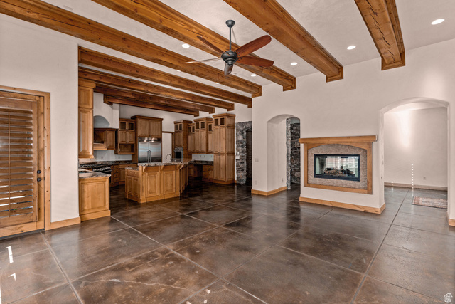 2464 East Granite Way St. George, UT 84790 - Photo 44 of 106 Kitchen featuring beamed ceiling, a kitchen island with sink, ceiling fan, glass insert cabinets, and a multi sided fireplace