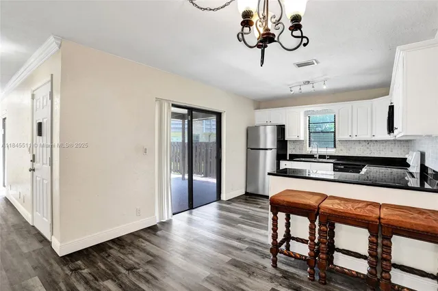 a kitchen with stainless steel appliances granite countertop a refrigerator a sink dishwasher a dining table and chairs with wooden floor