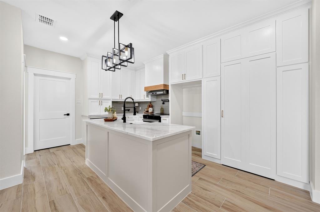 120 Springwood Road Enchanted Oaks, TX 75156 - Photo 21 of 37 Kitchen featuring an island with stone countertop, white cabinetry with crown molding, wood-finish flooring, and a modern light fixture