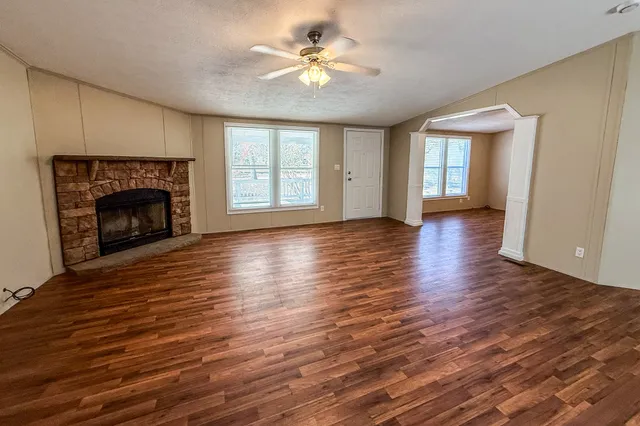 a view of an empty room with wooden floor fireplace and a window
