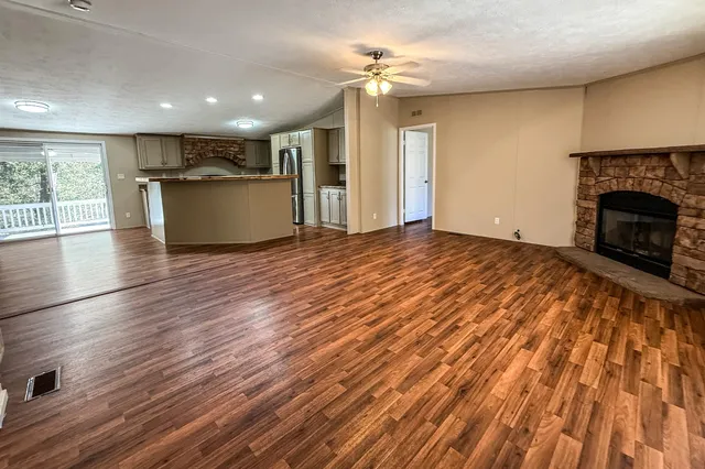 a view of a livingroom with a fireplace a ceiling fan and wooden floor