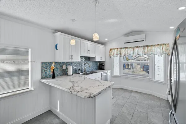 a large white kitchen with granite countertop a stove a sink a refrigerator and white cabinets with wooden floor