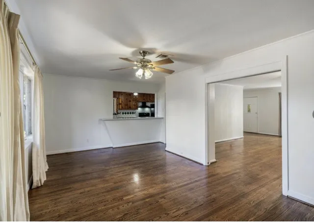 an empty room with wooden floor chandelier fan and windows