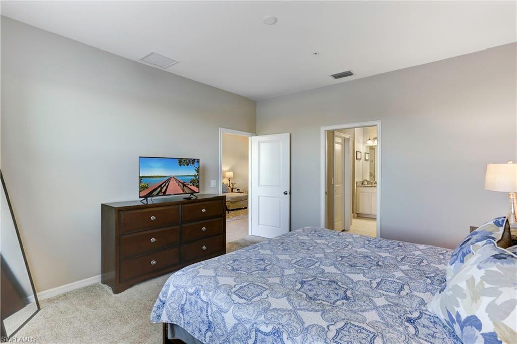 9433 Benvenuto Court, Unit 201 Naples, FL 34119 - Photo 13 of 32 a bedroom with a bed and a mirror