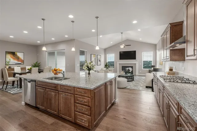 a kitchen with stainless steel appliances granite countertop a stove top oven a sink dishwasher a dining table and chairs with wooden floor