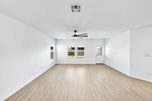 an empty room with wooden floor chandelier fan and windows