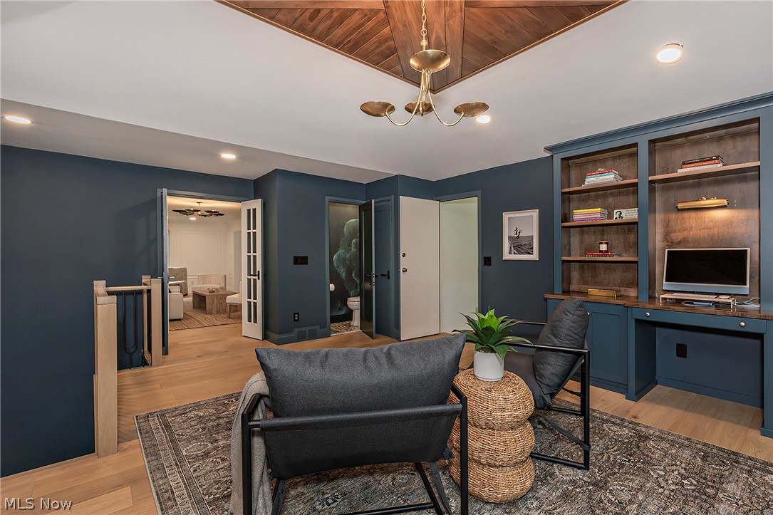3189 Lander Road Pepper Pike, OH 44124 - Photo 13 of 43 Hardwood flooring throughout, featuring a built-in office desk and shelving, a decorative brass chandelier, a wood-paneled ceiling accent, and built-in wall cabinetry