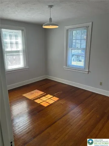 an empty room with wooden floor chandelier fan and windows