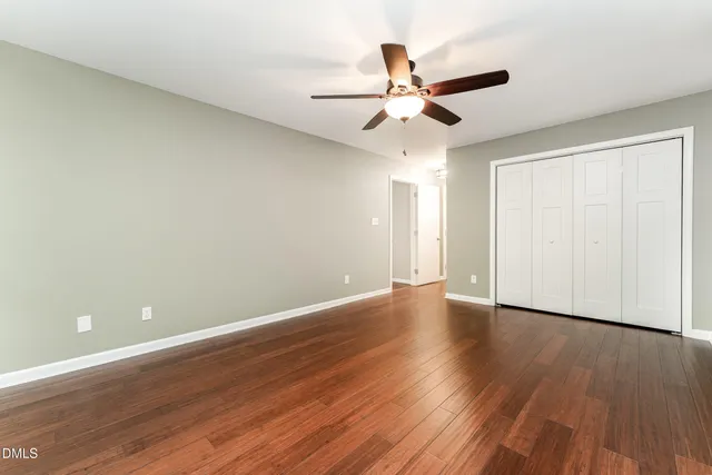 a view of an empty room with wooden floor and a ceiling fan