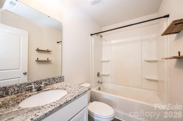 a bathroom with a granite countertop bathtub shower sink vanity mirror and toilet