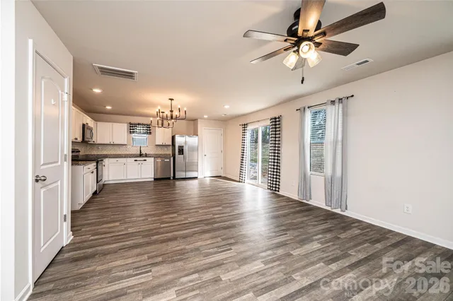 a view of an empty room with wooden floor and a kitchen