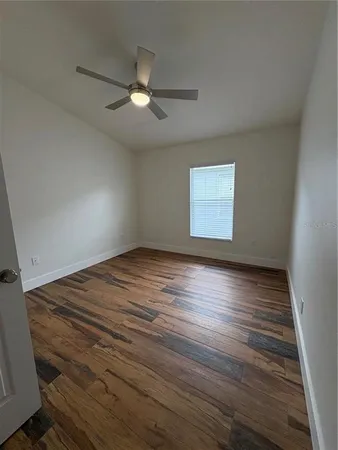 an empty room with wooden floor chandelier fan and windows