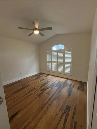 an empty room with wooden floor chandelier fan and windows