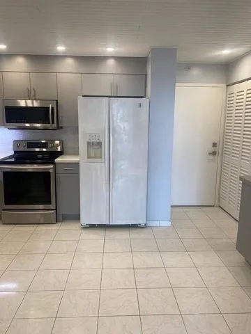 a view of a refrigerator in kitchen and empty room with wooden floor