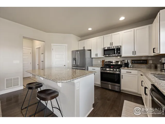 a kitchen with stainless steel appliances granite countertop a stove a sink a microwave a refrigerator and white cabinets